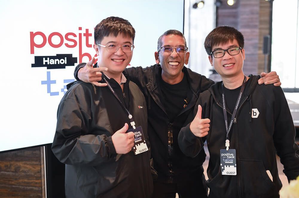 Three attendees pose in front of the Positive Hack Talks Hanoi screen
