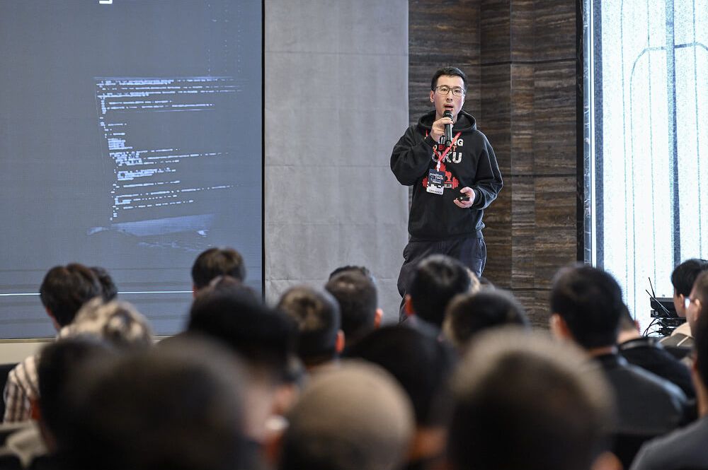 A speaker on stage in front of a slide of code, the audience in the foreground